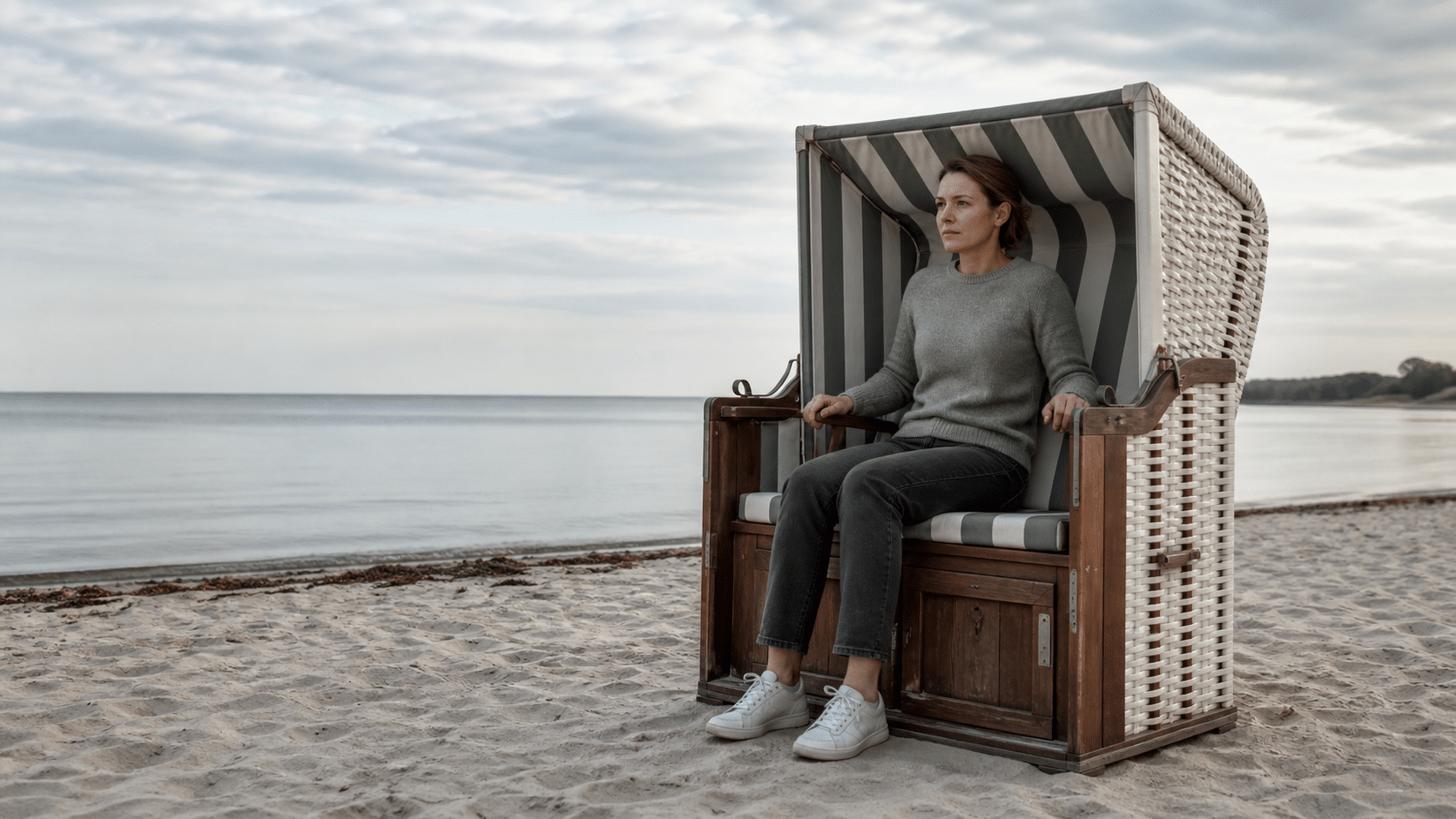 Warum Erholung bei emotionaler Erschöpfung nicht mehr wirkt: Frau sitzt angespannt im Strandkorb am leeren Ostseestrand